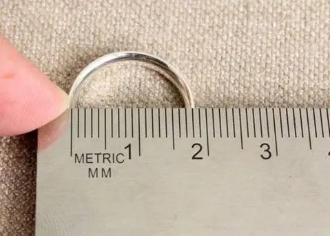A person is holding a measuring tape alongside a ring, likely measuring for a proper fit or size.