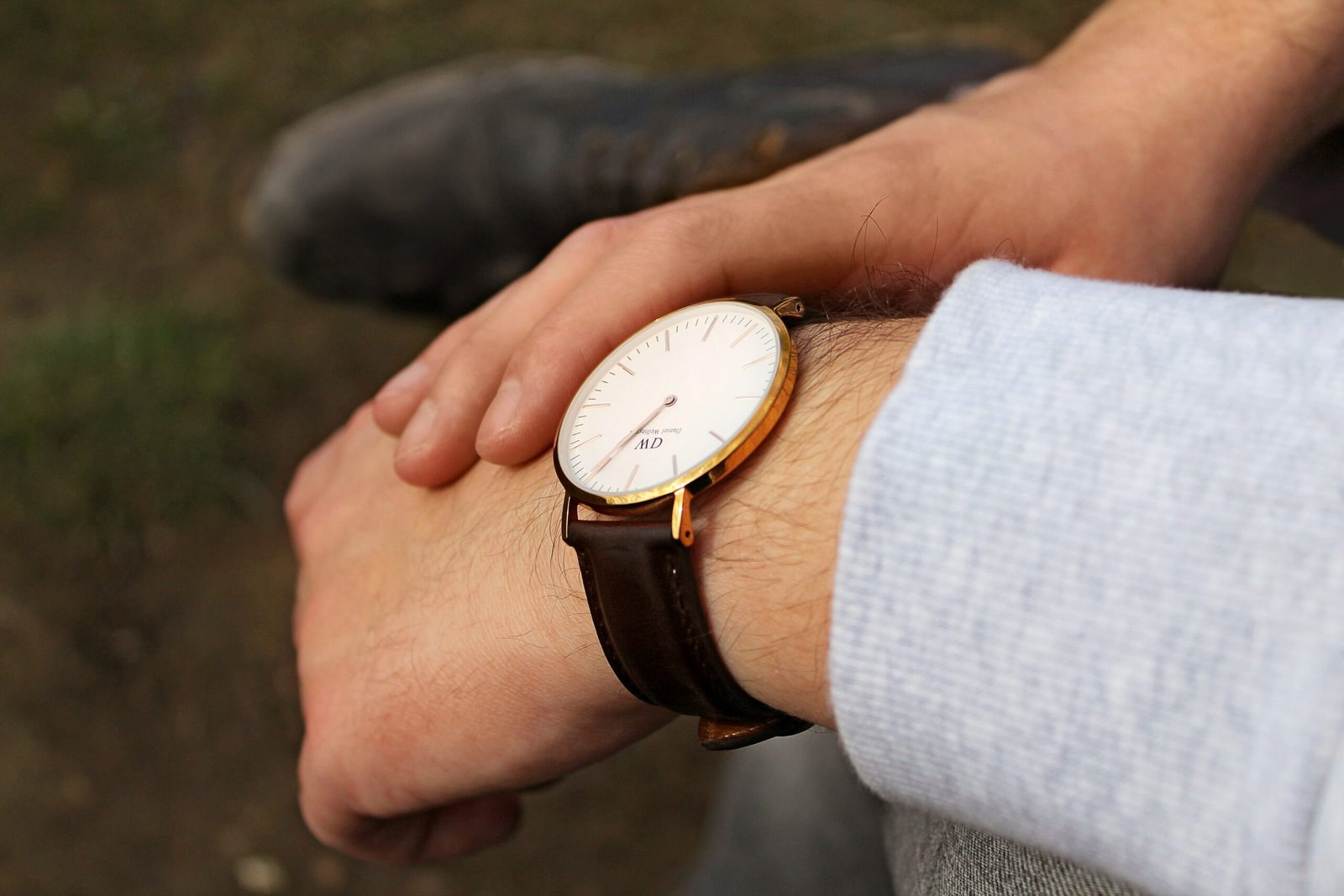Close-up of a man’s wrist wearing a minimalist white dial dress watch with a brown leather strap.