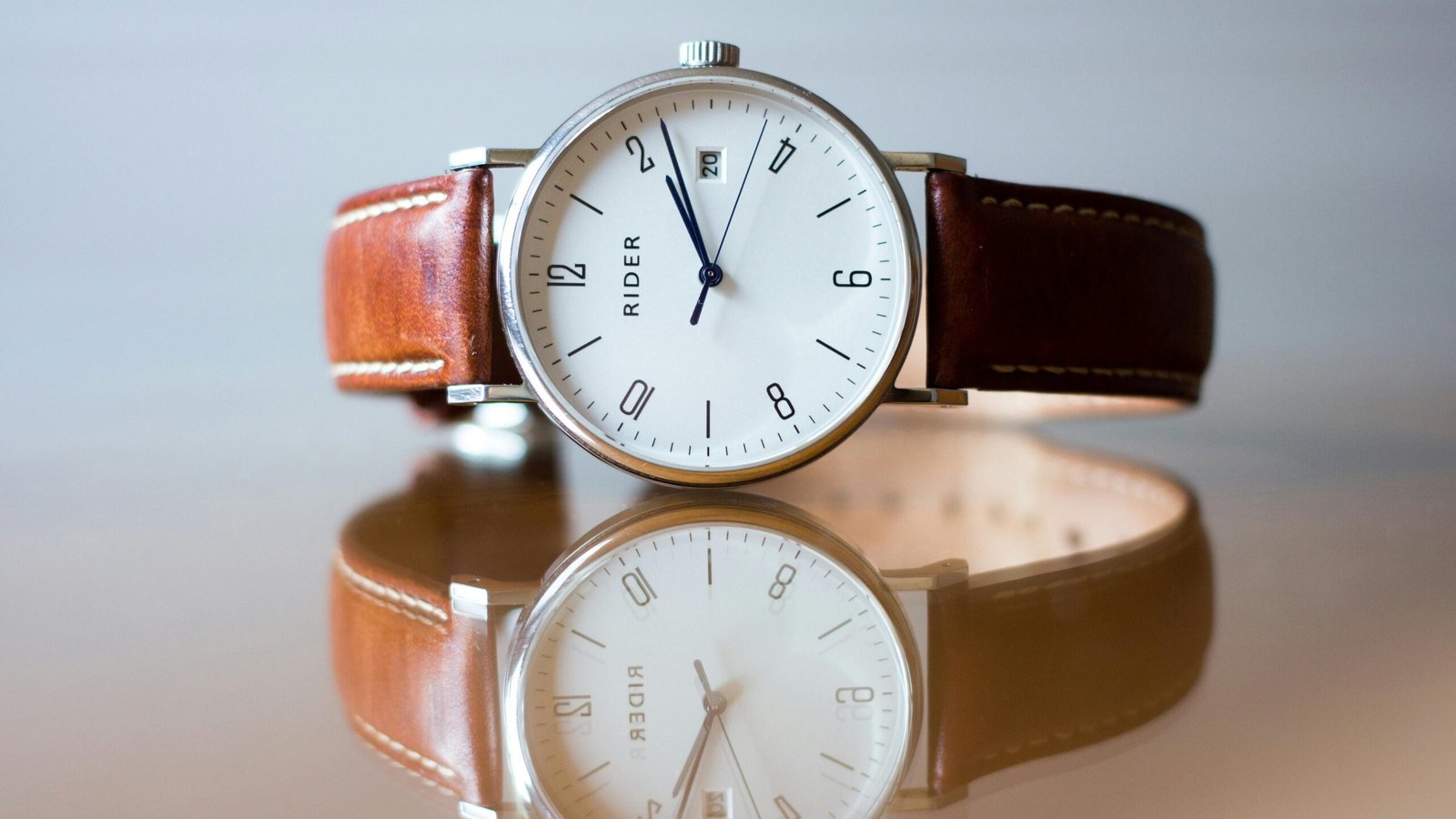Close-up of wrist minimalist white dial dress watch with a brown leather strap.